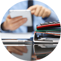 Man using ipad at desk with stack of notebooks, papers and calculator